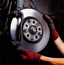 Hands wearing red gloves adjust a brake after coupons and discounts used for brake servces in Pompano Beach