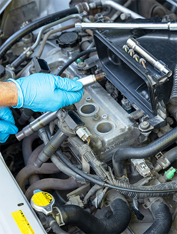 Gloved hands check wire connection to the car battery during yearly auto maintenance