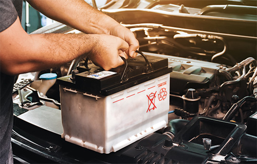 A car battery is held by a mechanic during car battery replacement in Pompano Beach