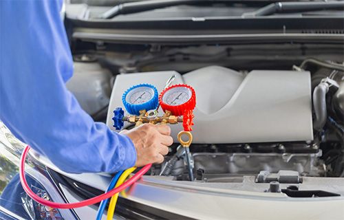 A mechanic in a blue shirt attaches gauges to check air conditioning in Pompano Beach