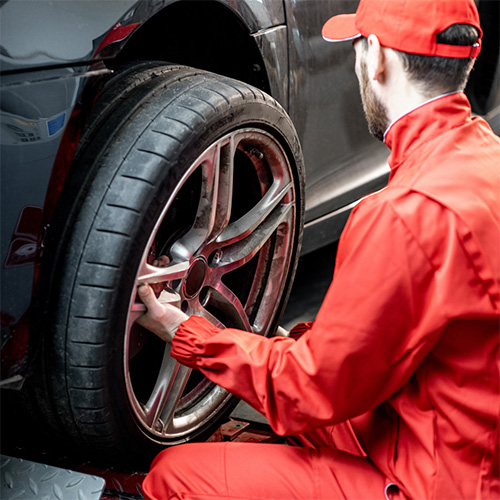 Mechanic in a red jumpsuit holds a new tire in place during new tire installation
