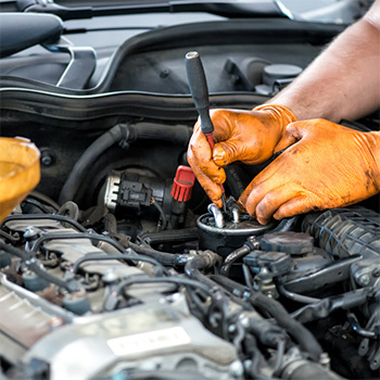 Gloved hands work under a car hood for regular auto maintenance in Pompano Beach